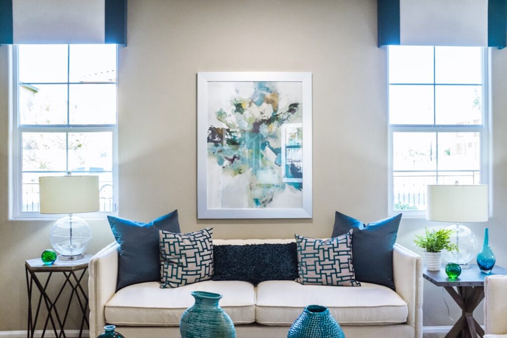A person holds paint swatches against a living room wall with natural light streaming in.