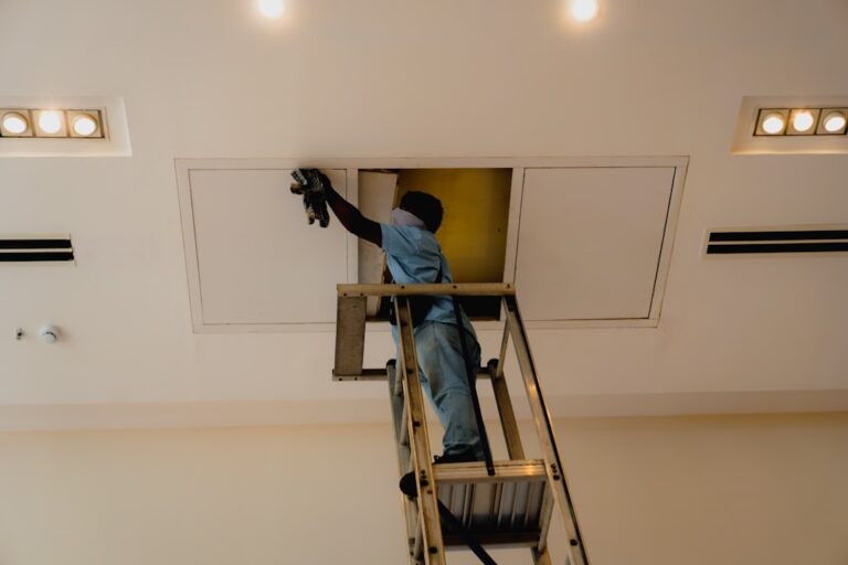 Person rolling white paint across a ceiling while walls and floor are covered with protective sheeting